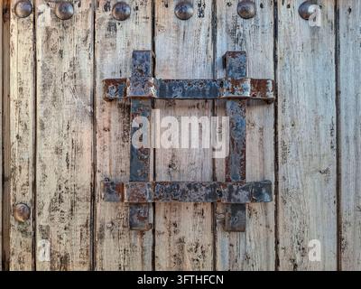 Close-up full-frame view of an antique wrought iron window grille or peephole grate mounted on an old, weathered wooden door. The composition highligh Stock Photo