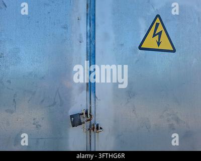 A straight-on view of a closed galvanized steel electrical cabinet secured with a padlock on the center latch. The upper right door features a promine Stock Photo