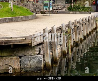 Weathered wooden dock supports and stone retaining wall reflected in fjord water  Stock Photo