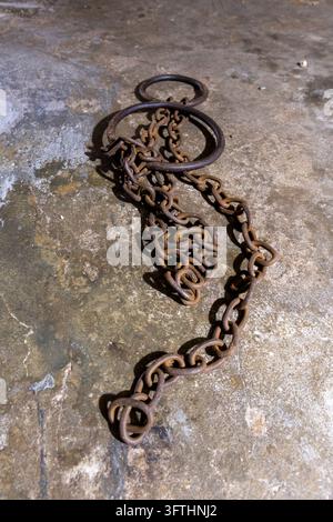 Rusty iron chain and rings coiled on a rough stone floor at the East Africa Slave Trade Exhibition museum site, Stone Town, Tanzania Stock Photo