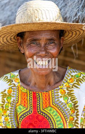 Portrait of a smiling elderly woman in a straw hat and a colorful traditional top in front of a thatched hut, Menabe, Tsiribihina, Madagascar Stock Photo