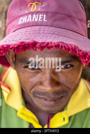 Close portrait of a man wearing a pink Chanel hat and a green and yellow shirt, Menabe, Morondava, Madagascar Stock Photo