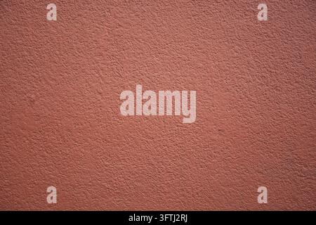 A full-frame close-up shot showing a wall with a flattened, rough stucco or plaster finish, painted in a uniform shade of rust orange, terracotta, or Stock Photo