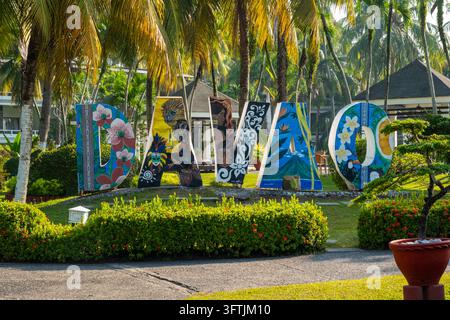 A large decorative sign stands among palm trees and garden plants at a tropical resort in Davao, Philippines, during daylight. Stock Photo