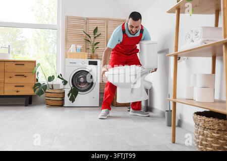 Plumbing services and home renovation, professional plumber installing a new toilet in a modern bathroom interior with laundry appliances and decor Stock Photo