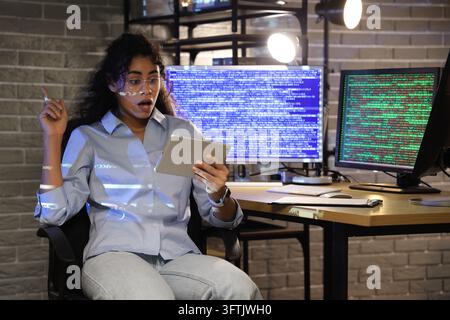 Software development breakthrough, female programmer feeling excited while looking at tablet with code projection in dark office at night Stock Photo