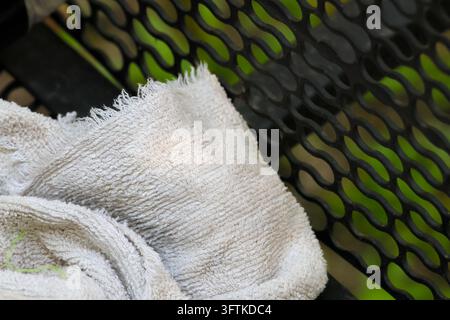 A white terry cloth towel draped over black green mesh surface with soft texture and curved folds in close up composition Stock Photo