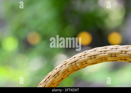 A woven basket handle curves across garden scene with golden bokeh and lush green foliage, creating calm outdoor background with detailed natural fibe Stock Photo