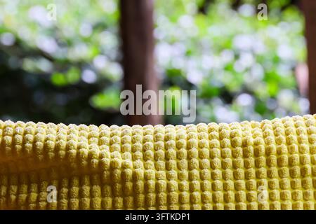 A yellow textured fabric with raised waffle pattern in soft focus, photographed outdoors against sunlit green forest background with warm natural ligh Stock Photo