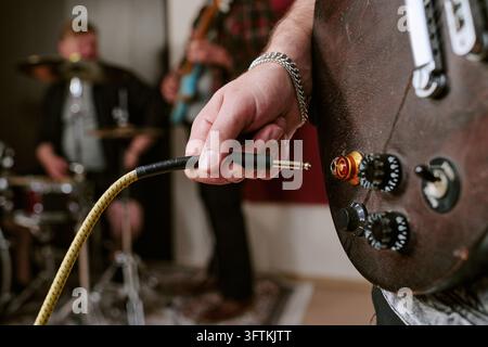 Musician Plugging Audio Cable into Electric Guitar during Band Rehearsal Stock Photo
