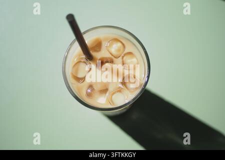 Iced drink with a straw sitting on a green table surface in sunlight Stock Photo