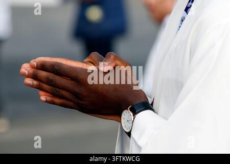 A close-up of the clasped hands of a priest in a white alb as he prays during Mass. Stock Photo