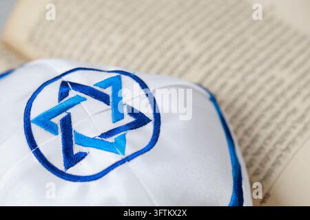 A white kippah with a blue Star of David rests gently on the open pages of this holy book, illustrating Jewish tradition. Stock Photo