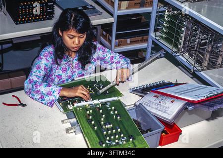 In Malaysia, a factory worker carefully assembles electronic components onto printed circuit boards in a production workshop. Stock Photo