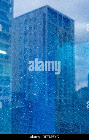 Close-up of a heavily shattered and cracked glass window in Espoo, revealing a blurred view of a modern skyscraper through the web of broken fragments Stock Photo