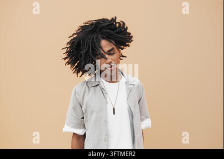 Young black man with closed eyes, feeling the movement of his twist braids on a plain background Stock Photo