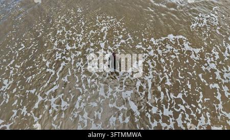 Aerial drone view of Antony Gormley Another Place iron man sculpture in foaming waves at Crosby Beach, Merseyside, England Stock Photo