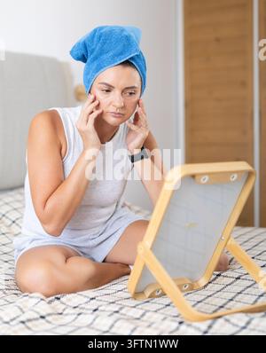 Adult woman looking into mirror sitting on bed Stock Photo