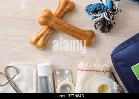 Flat lay of dog care items including bones, rope toy, bandages, scissors, and medical supplies arranged on a light wooden background. Stock Photo