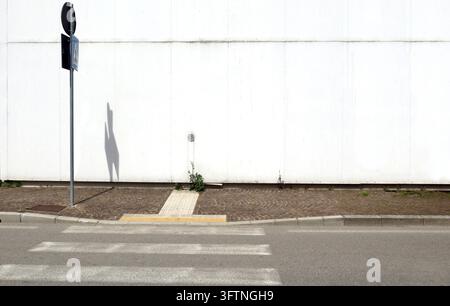 Weathered white concrete wall with air intake. Sidewalk, pedestrian crossing sign, crosswalk and urban street in front. Background for copy space. Stock Photo