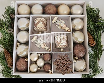 Top view of an open box filled with elegant Christmas tree ornaments in champagne, ivory and rose gold tones. Decorative baubles, nutcracker figures, drums and a glittering snowflake. Stock Photo