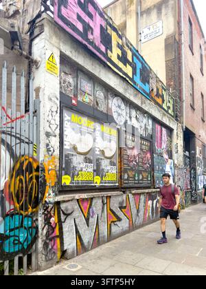 Person walking past building with graffiti and Henry Moore posters in Brick Lane, London Stock Photo