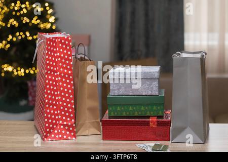 Christmas Gift Boxes and Shopping Bags on Table with Illuminated Christmas Tree in Background Stock Photo