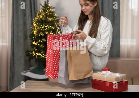 Young Woman Holding Christmas Shopping Bags Near Decorated Tree and Gift Boxes at Home Stock Photo