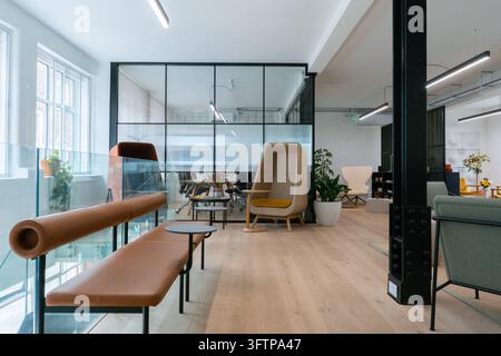 View of Office Mix, a modern open-plan office interior featuring contemporary furniture, glass partitions, and light wooden flooring in London, United Stock Photo