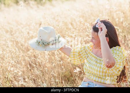 Smiling mature woman holding floral straw hat in sunny meadow, expressing happiness, freedom, relaxation and carefree summer lifestyle Stock Photo