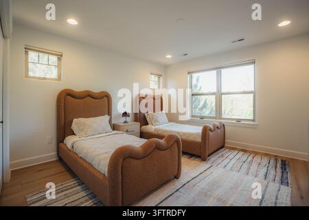 Twin bedroom with two upholstered brown beds placed side by side, matching headboards and footboards, white quilted bedding, single wooden nightstand Stock Photo