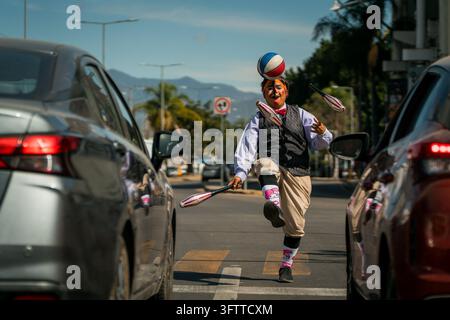 Mexico - 28 January 2025: View of a street performer juggling clubs and a ball on his head while standing in the middle of a street between cars. Stock Photo