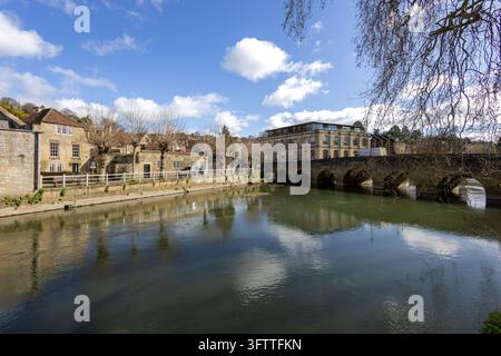 A multi-arched stone bridge crosses a calm river beside honey-coloured town buildings. Stock Photo