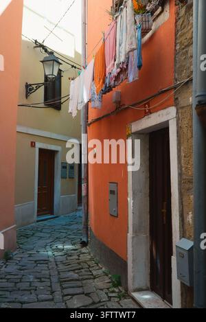 Narrow stone alley with orange painted walls, street lamp, and laundry hanging on clothesline in Piran, Slovenia. Stock Photo