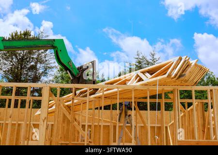 Crane is lifting wooden trusses beams to top of building frame on residential construction Stock Photo