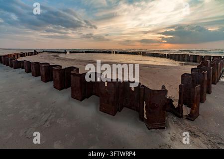 A detailed shot focusing on the textured corners of a rusty metal sheet piling structure standing on a sandy coast by the ocean at golden sunset. Stock Photo