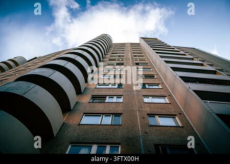 A low-angle view looks up the facade of a tall residential building with stacked curved balconies and rows of rectangular windows. Strong converging l Stock Photo