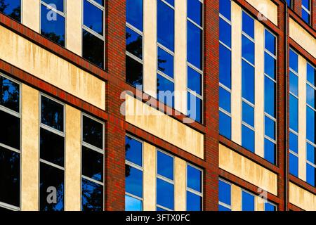 Tall windows reflect blue sky and swirling white clouds across a yellow building facade. Red brick columns and horizontal bands frame the textured wal Stock Photo