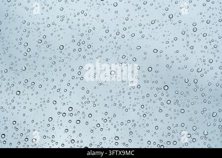 Raindrops falling and trickling down window glass on blue background Stock Photo