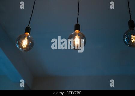 Three vintage Edison filament bulbs hanging from black cables against a moody blue-grey ceiling Stock Photo