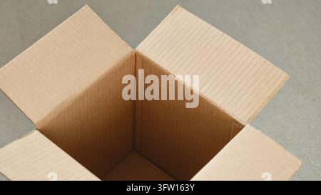 An open empty cardboard box sits on a neutral textured surface. Close up. Stock Photo