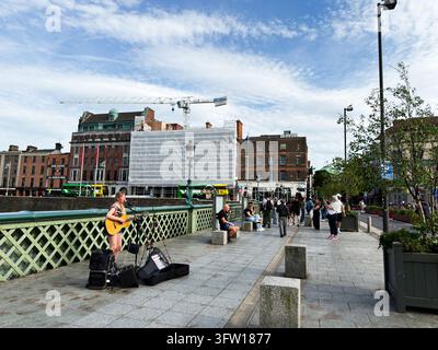 Dublin, Ireland - May 23, 2026: Young busker plays acoustic guitar on a Liffey bridge as pedestrians and tourists gather in Dublin, Ireland. Stock Photo