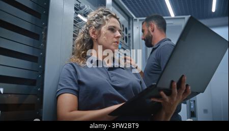 IT Specialists Review Server Performance on Laptop While Discussing Metrics and Adjusting LED Indicators, Demonstrating Collaboration, System Monitoring, Configuration, and Infrastructure Control. Stock Photo