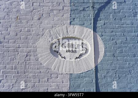 An oval white plaque with raised lettering and the date 1853 is set into a wall of white and pale blue painted brick in Hastings. Stock Photo