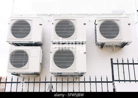Five outdoor air conditioning units mounted on a white building wall. HVAC equipment background for cooling systems, ventilation and building climate. Stock Photo