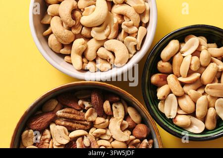 Top view of assorted nuts in separate bowls on yellow background. Cashews, peanuts and mixed nuts for healthy snacking and food selection. Stock Photo
