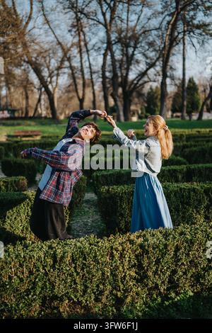Young couple playfully dancing and laughing in a hedge maze garden on a sunny day Stock Photo