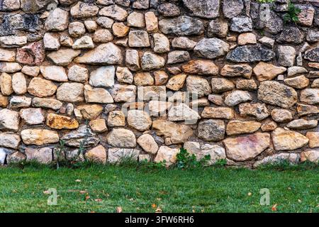 Old rustic natural stone wall background texture with green lawn grass at the bottom Stock Photo