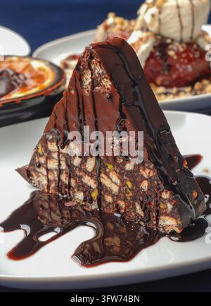 Pyramid Shaped Chocolate Mosaic Cake with Syrup and Pistachio on White Plate Stock Photo