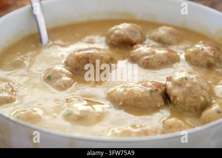 Close-up of a white bowl filled with delicious homemade meatballs smothered in a rich, creamy brown sauce, served with a spoon. Stock Photo